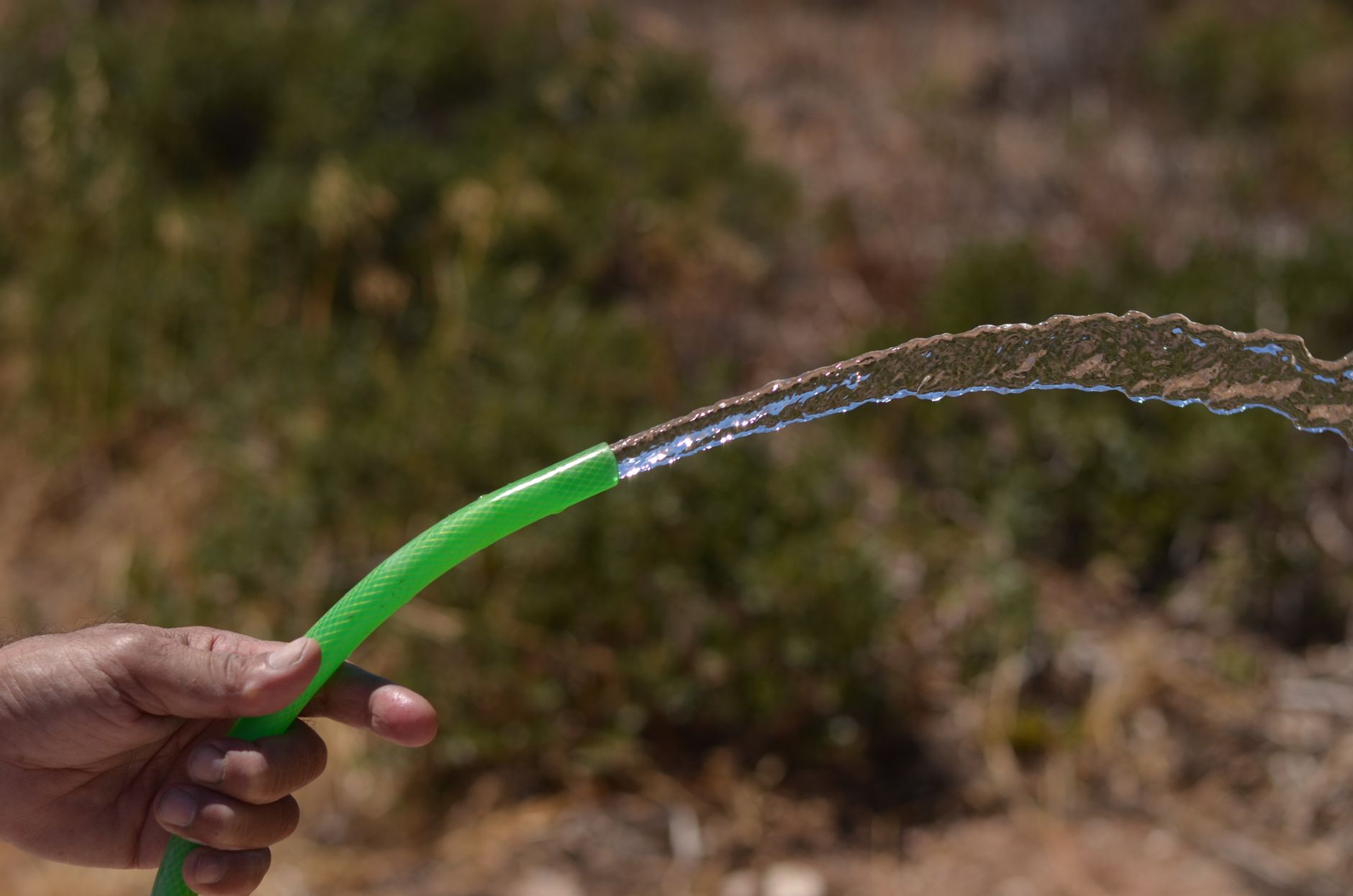 Close-up of liquid flowing from a garden hose outdoors, capturing motion.