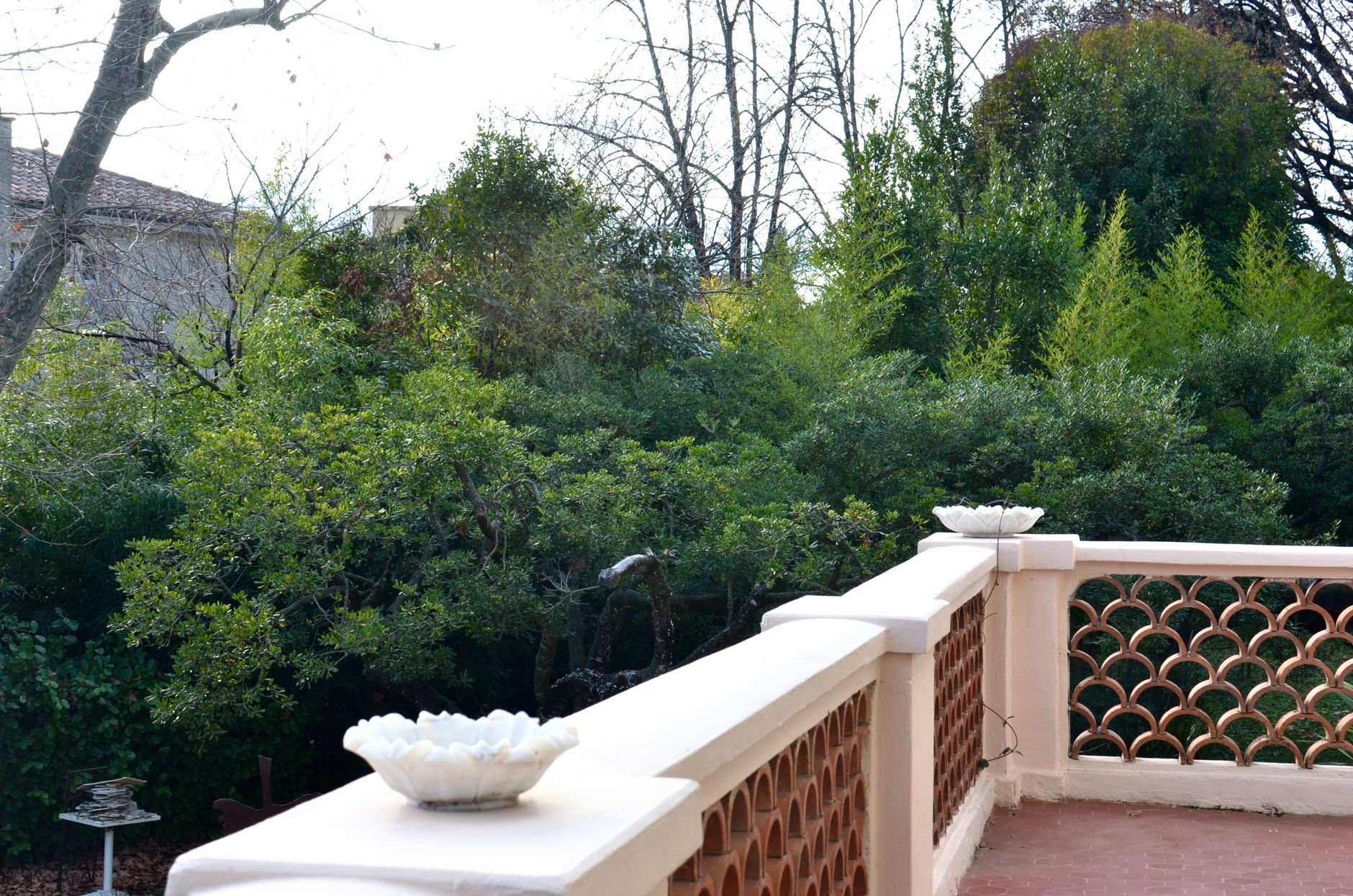 Picturesque view of tall green lush trees growing in yard from open white stone balcony in city