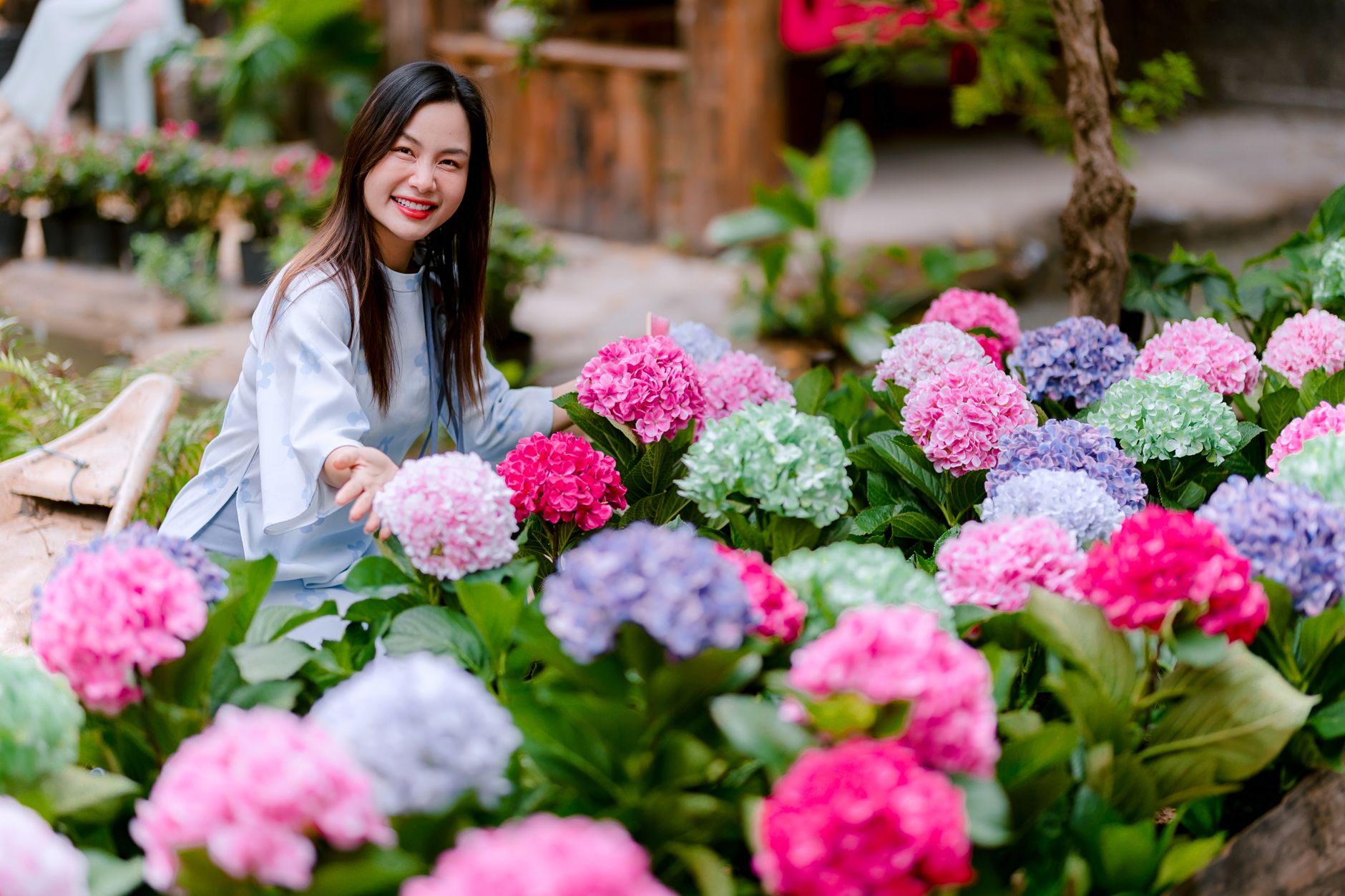 Woman smiling surrounded by colorful hydrangeas in a garden, capturing joy and natural beauty.