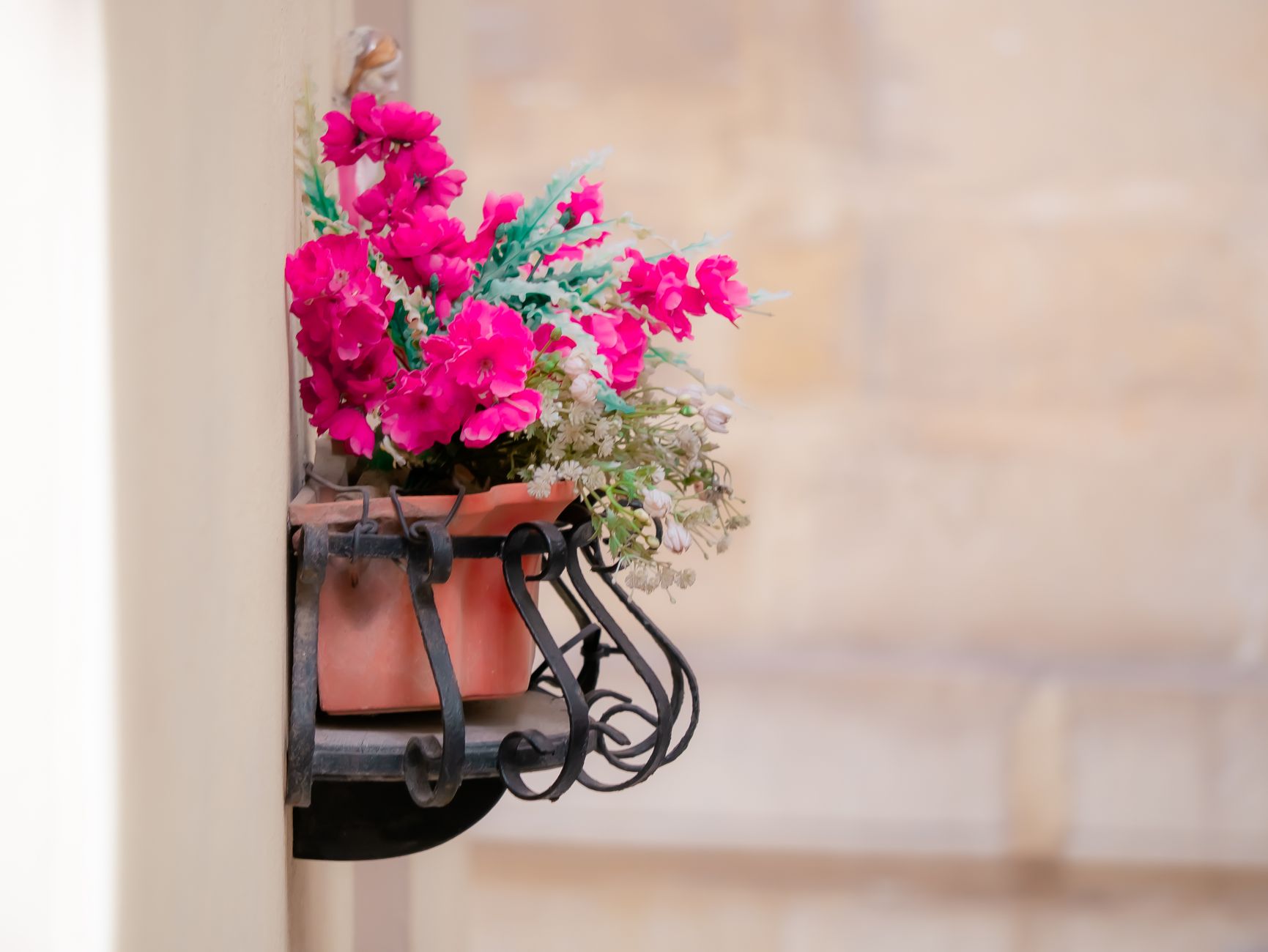 A vibrant floral arrangement in a terracotta pot, mounted on a decorative metal bracket.