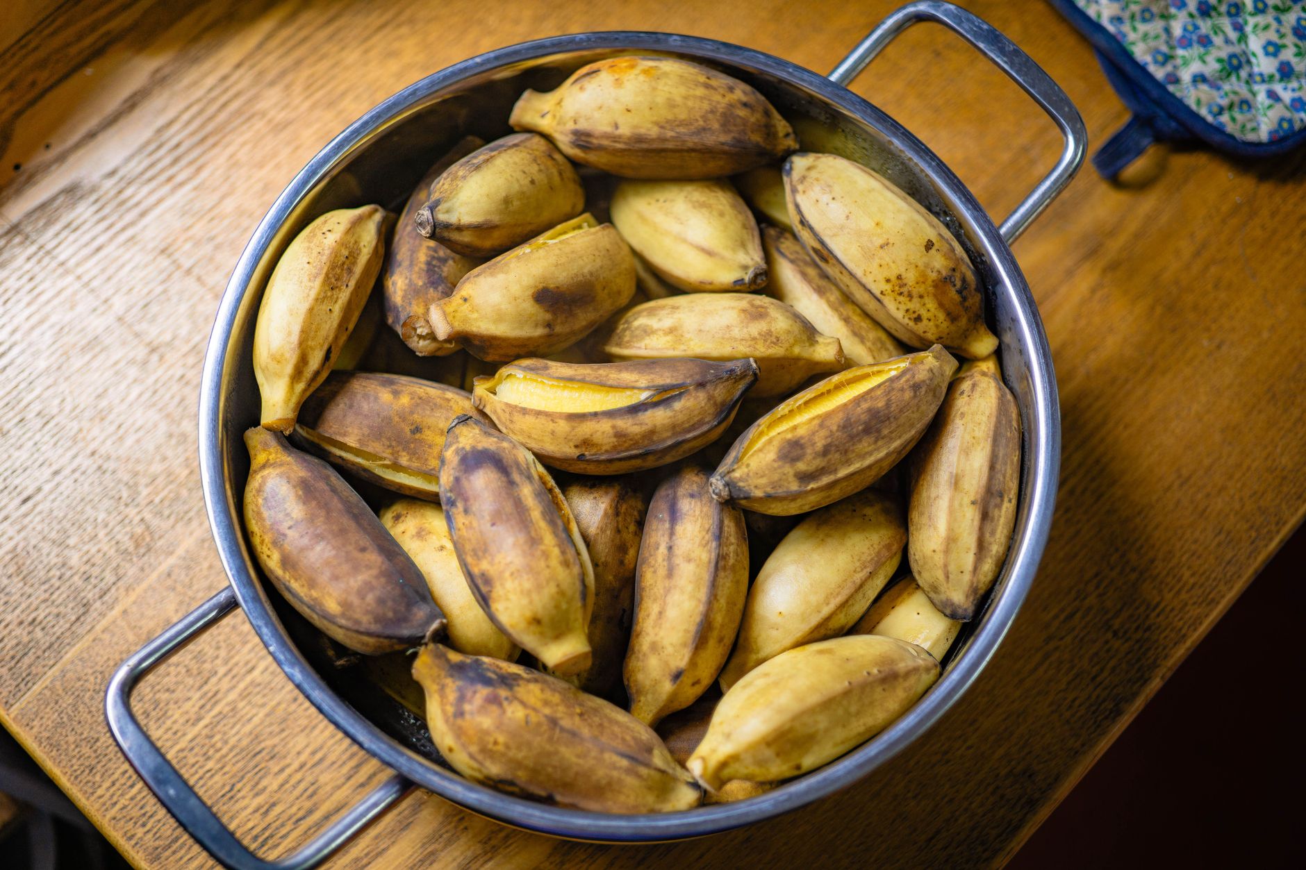 Ripe bananas in a large cooking pot on wooden table. Ready for cooking or baking.