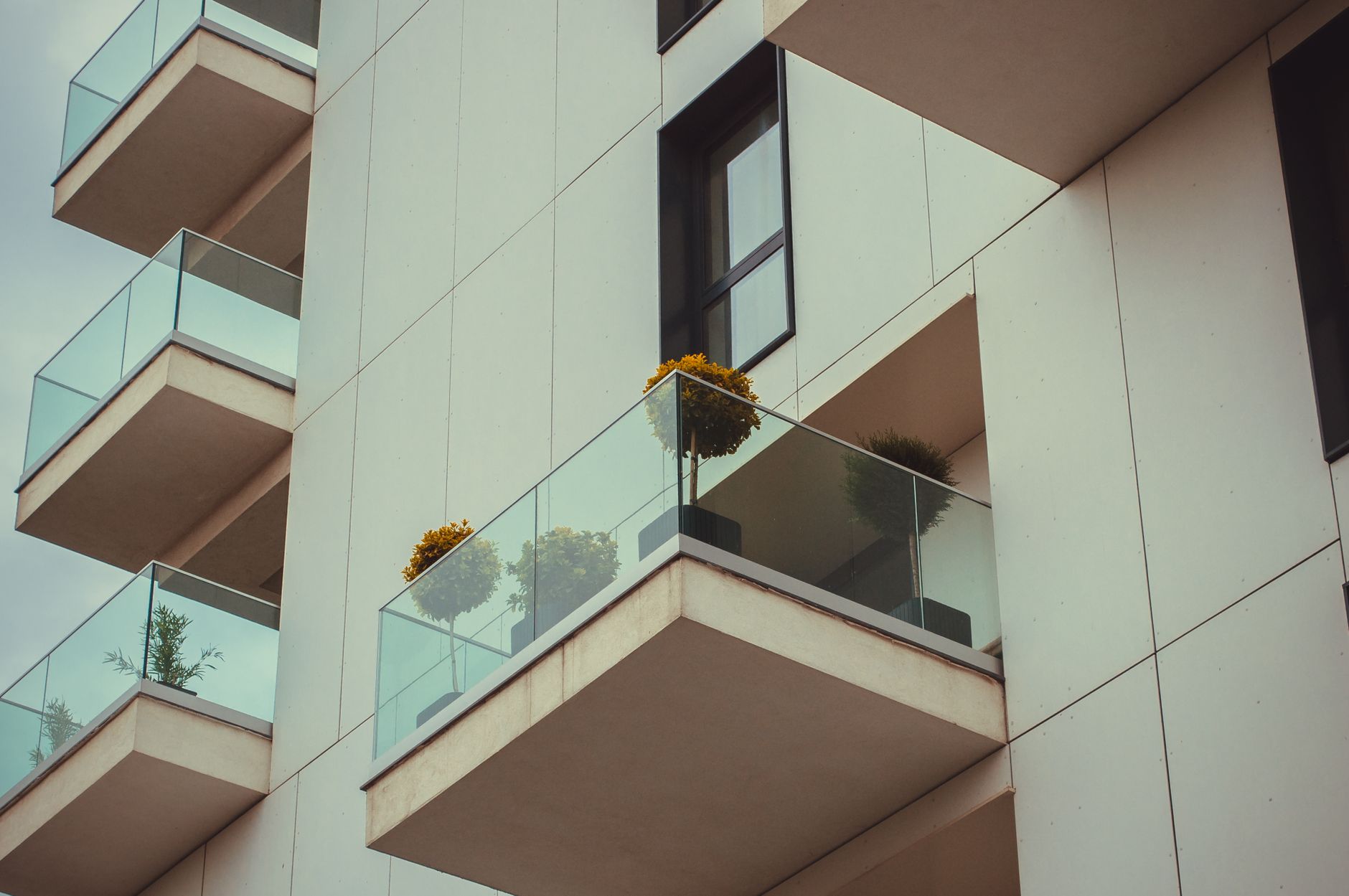A modern apartment building's glass balconies with potted plants create a sleek urban facade.