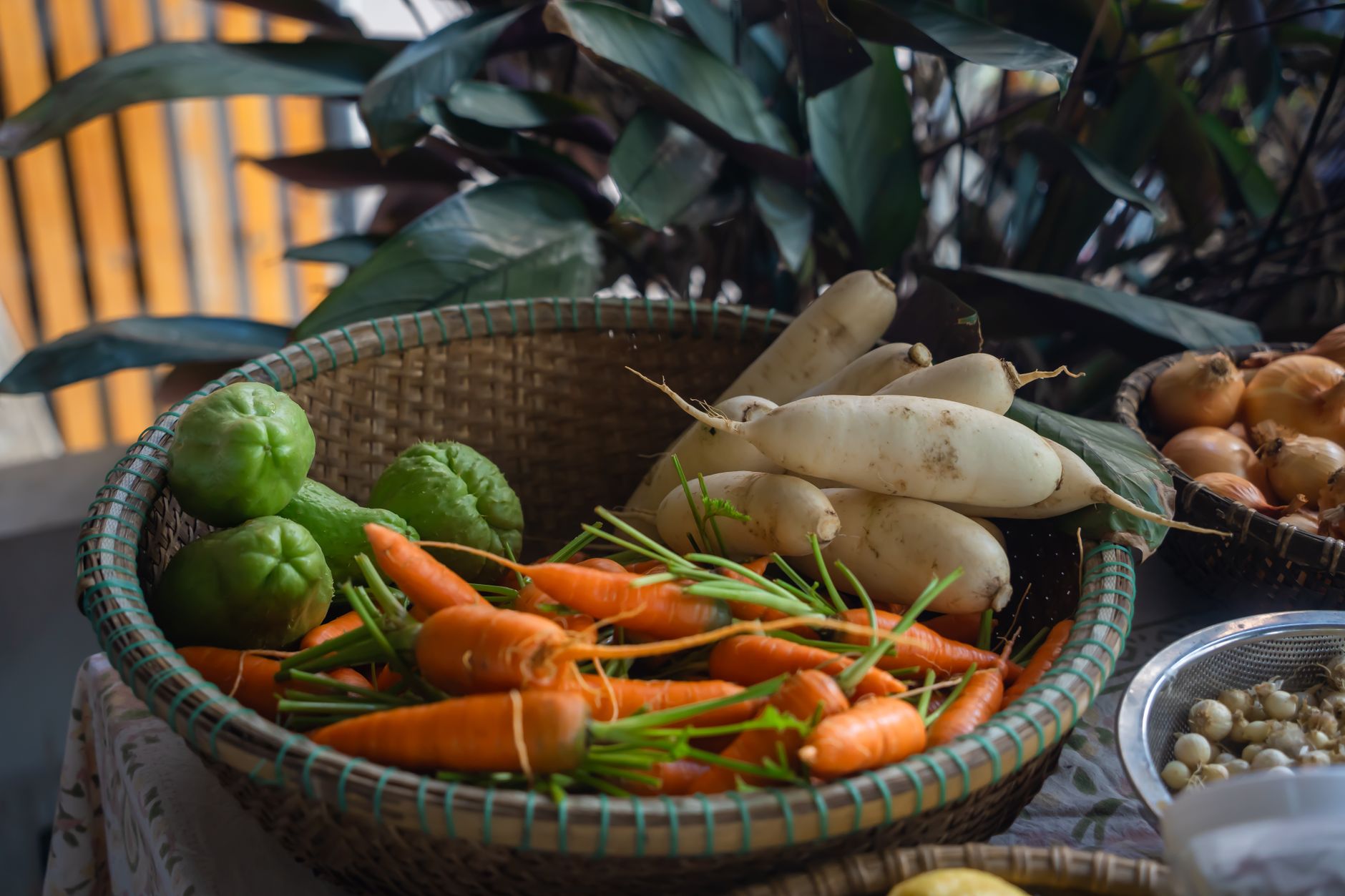 A variety of fresh vegetables including carrots, radishes, and chayote in a wicker basket.