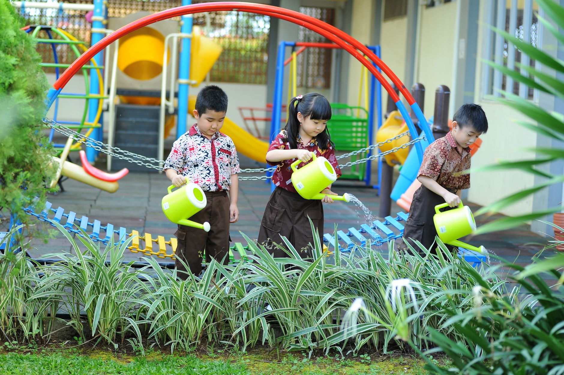 Young kids learning gardening skills by watering plants in a vibrant school playground setting.