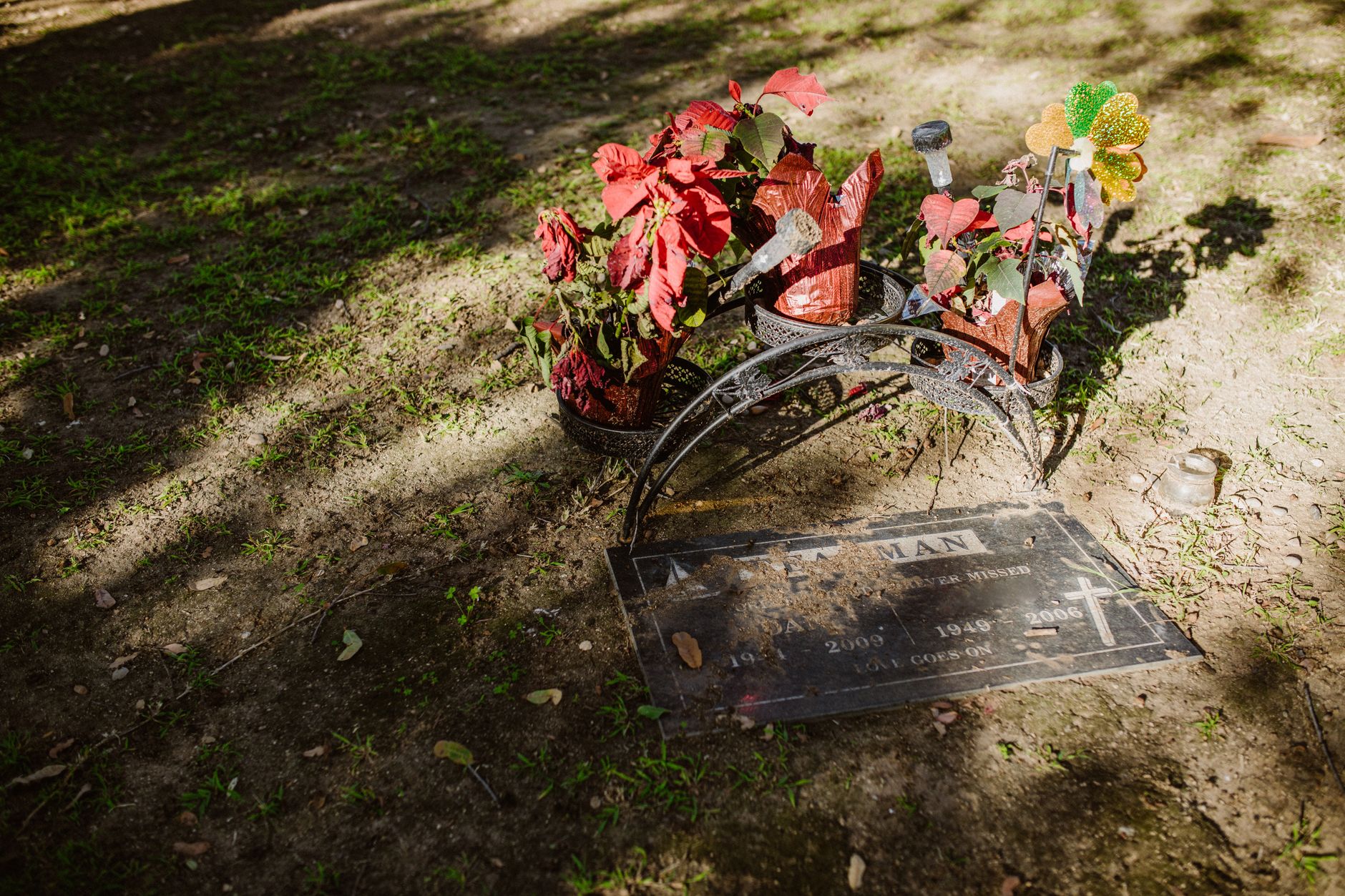 Peaceful grave adorned with vibrant red flowers and metal decorations in sunlight.