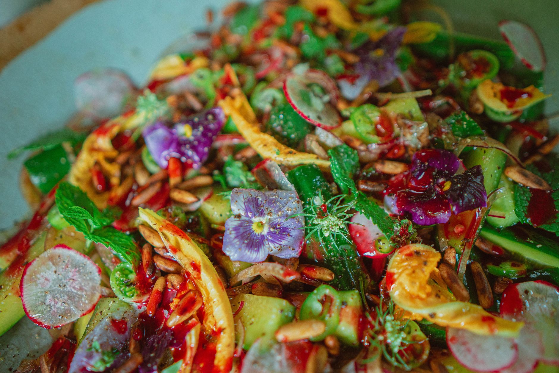 Colorful summer salad featuring edible flowers, fresh veggies, and nuts in a vibrant presentation.