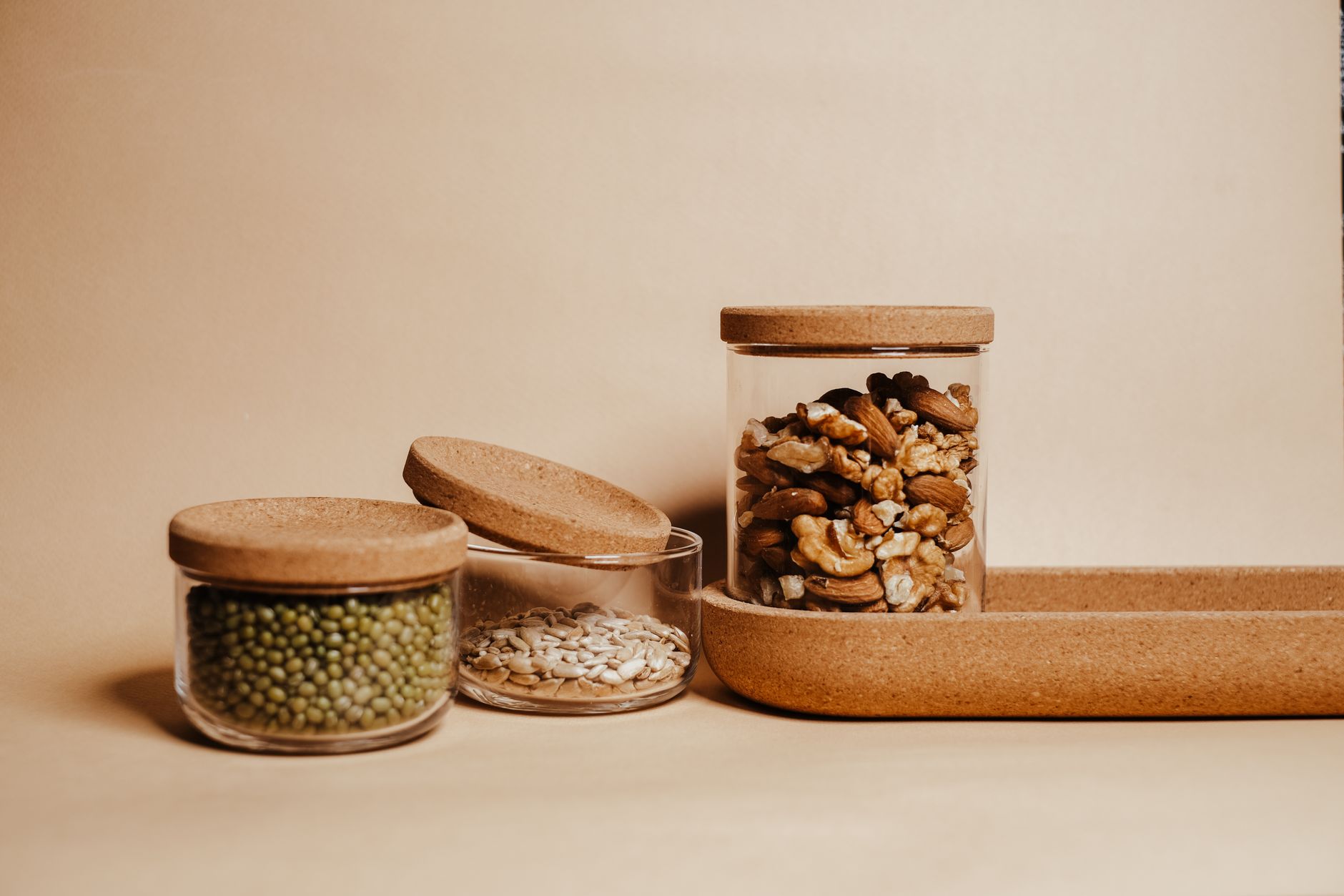 Assorted nuts and seeds in cork-lid glass jars on a wooden tray, showcasing organic storage.
