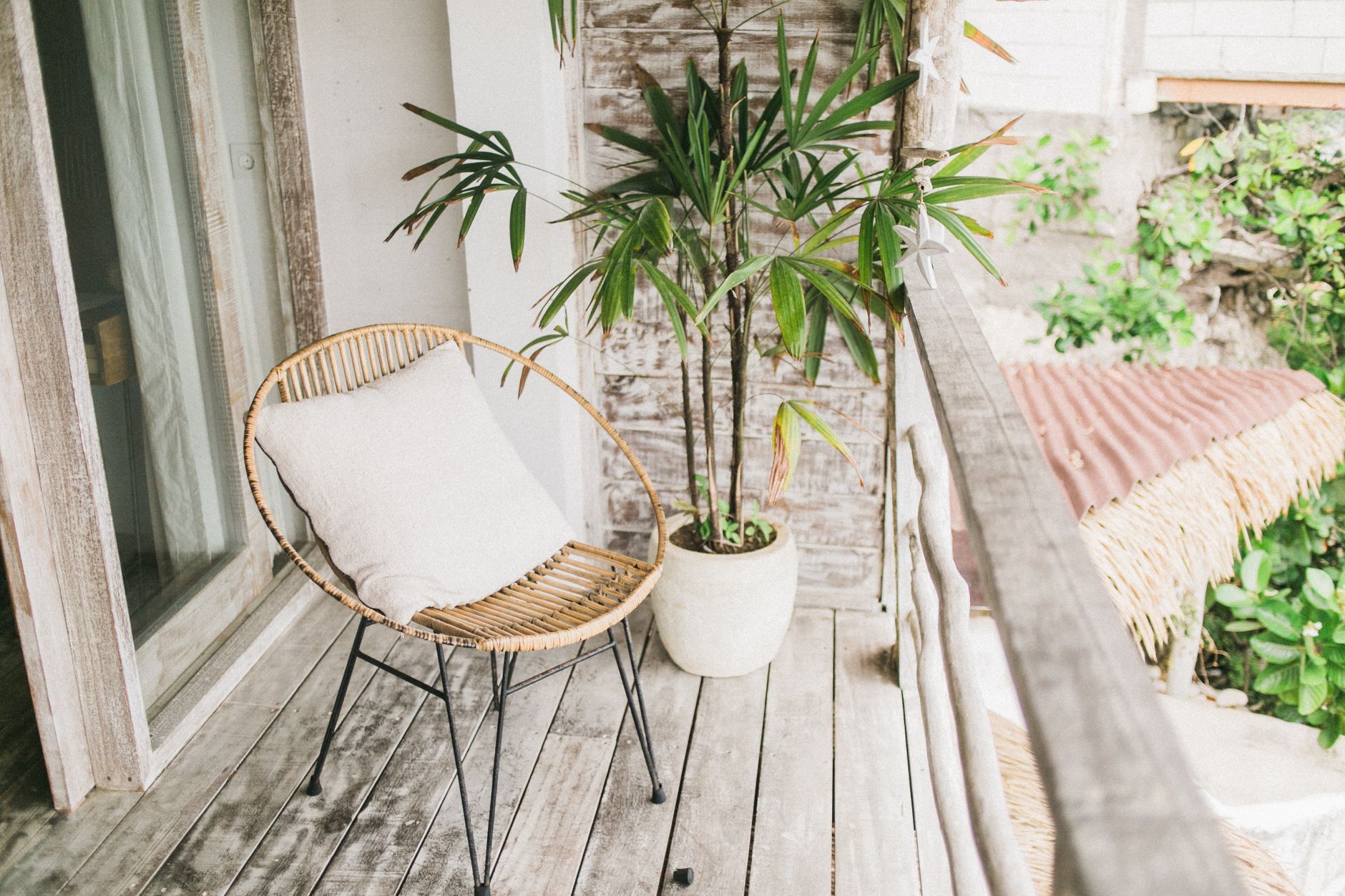 White cushion on small round lounger next to green plant in pot on balcony of wooden house in daytime