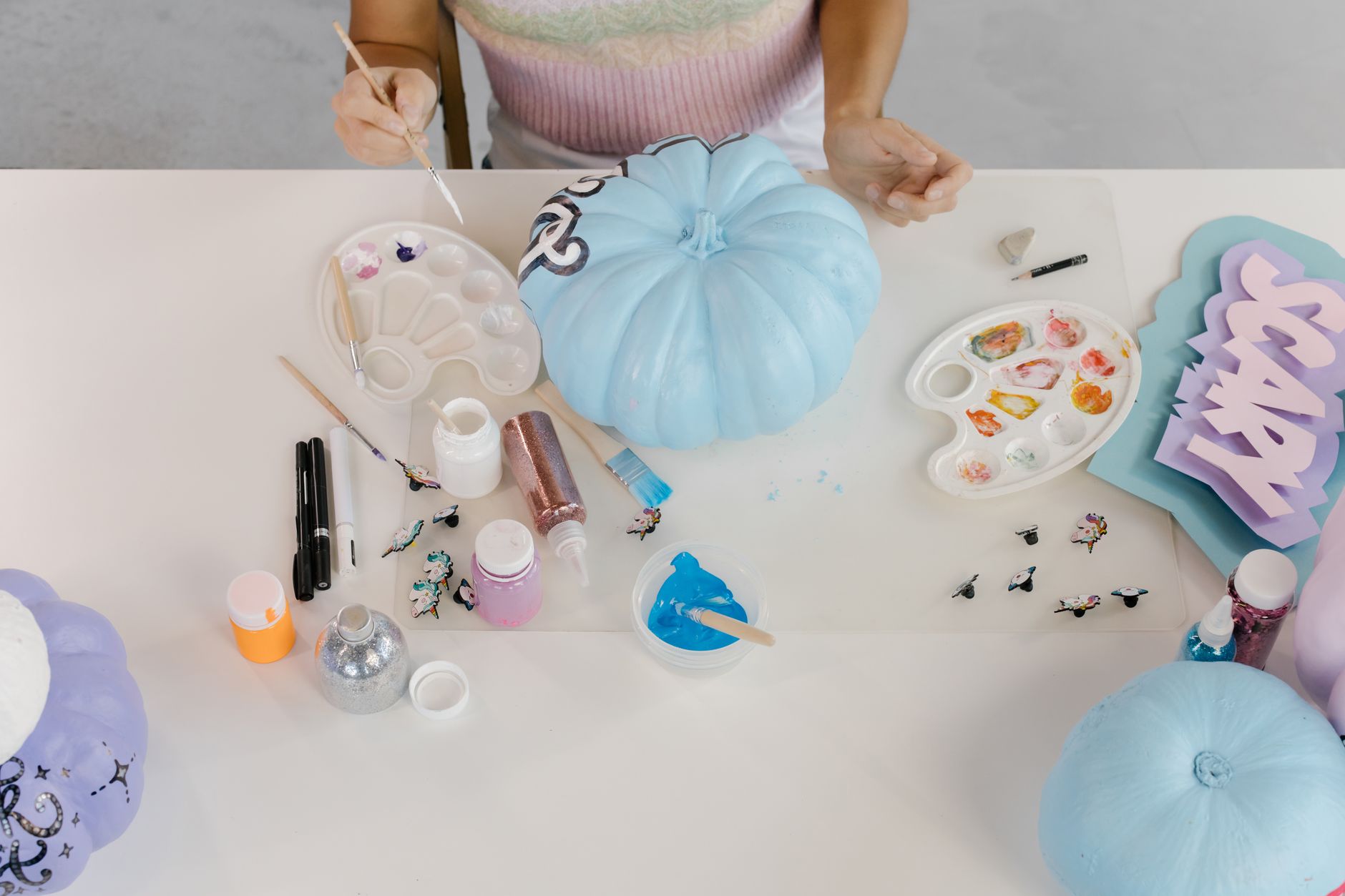A person painting pumpkins with blue paint for a Halloween decoration.